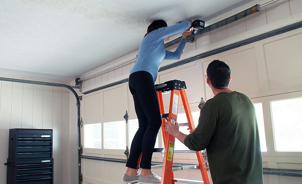 Homeowners inspecting garage door hardware with a drill